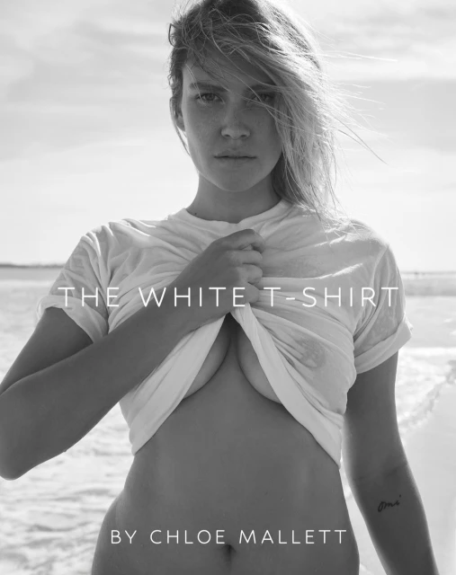Black and white portrait of a woman in a white t-shirt on a beach, with soft light and visible ocean waves in the background.