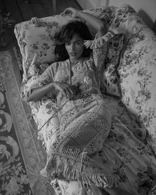 Black and white portrait of a woman lying on a floral bed wearing a crochet dress and holding a flower, artistic and elegant.
