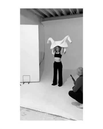 Behind-the-scenes photo by Chloe Mallett in New York showing a model taking off a white jacket in a studio.