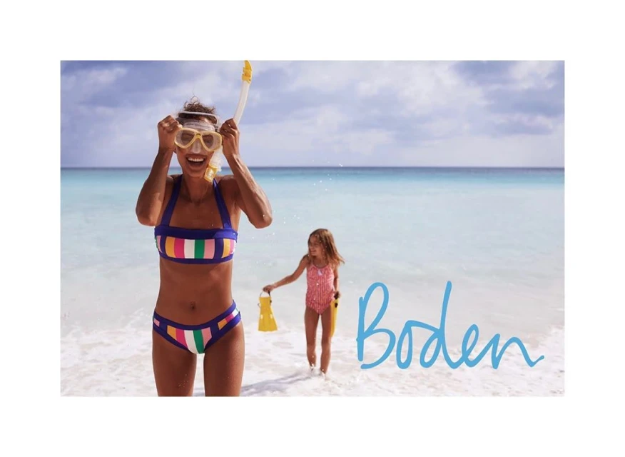 A woman and child in swimsuits are at the beach with turquoise water, the woman wearing a snorkel and mask, in a colorful outdoor shot.