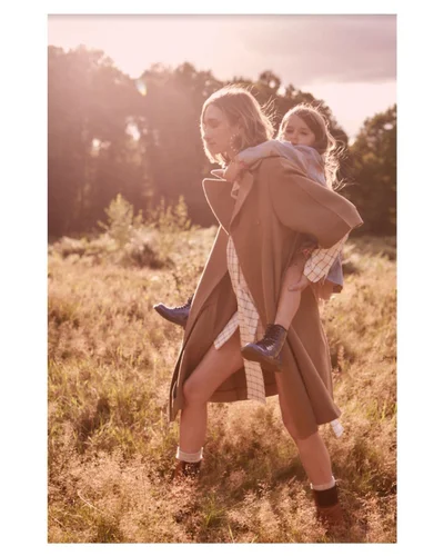 Woman carrying a young child on her back in a field during golden hour sunlight with lens flare
