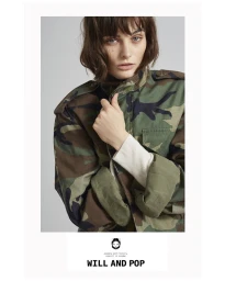 Model wearing a camouflage jacket against a grey background in a portrait photograph by Chloe Mallett