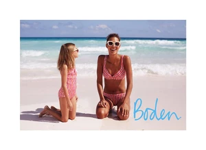 Two smiling females in matching patterned bikinis kneeling on a sandy beach by the ocean, captured by Chloe Mallett.