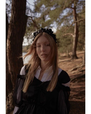 Woman wearing a black embellished headband and dark dress posing outdoors in a pine forest captured by Chloe Mallett