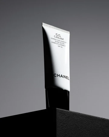 Still life studio shot of a white Chanel CC cream tube with black lettering, against a grey background on a black platform.