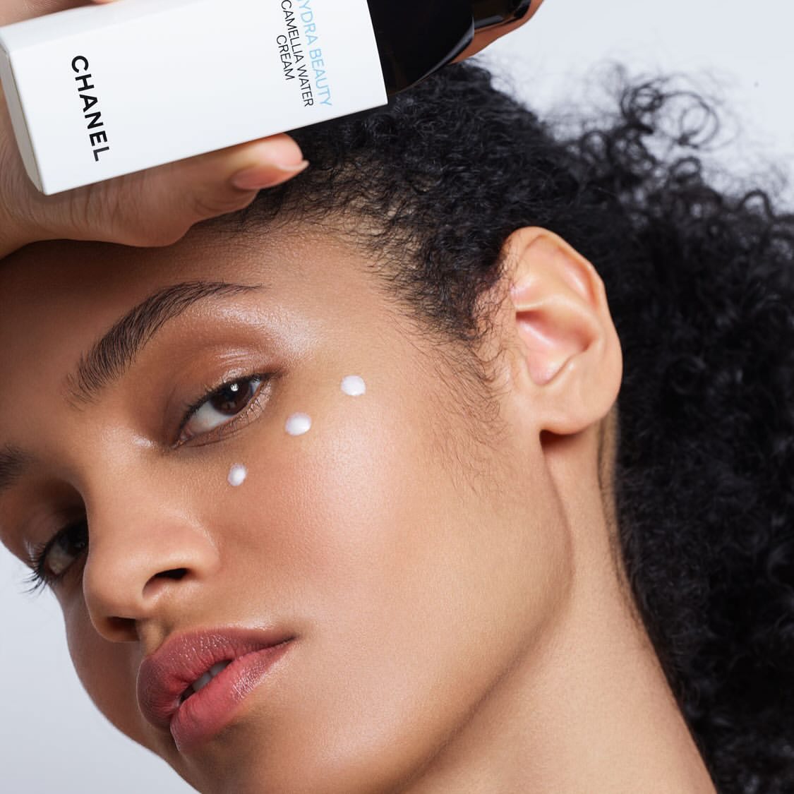 Close-up of a woman's face with skincare product dots, paired with a hand holding a Chanel Hydra Beauty Camellia Water Cream.