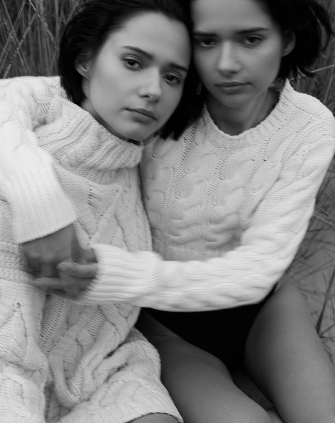 Monochrome close-up of two women embracing, wearing knit sweaters, with short dark hair, and blurred background. Beauty shot.