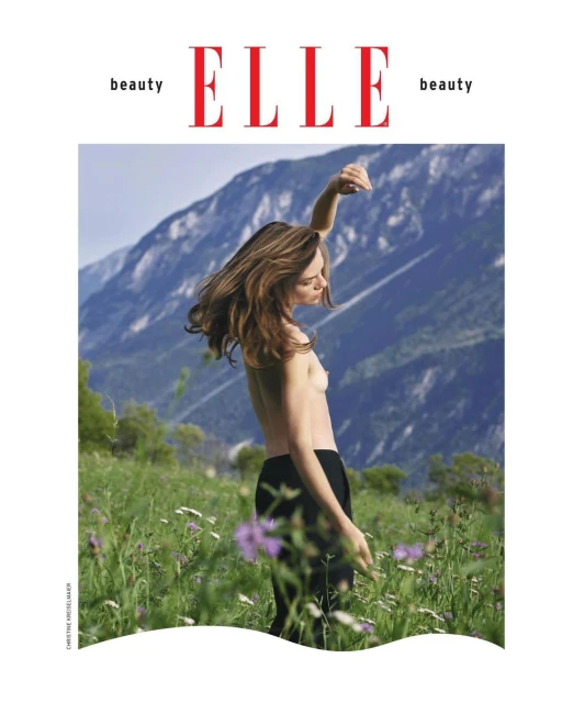 Magazine cover featuring a topless woman in black pants posing in a meadow with a mountain range in the background.