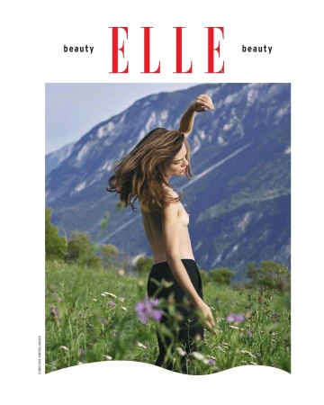 Magazine cover featuring a topless woman in black pants posing in a meadow with a mountain range in the background.