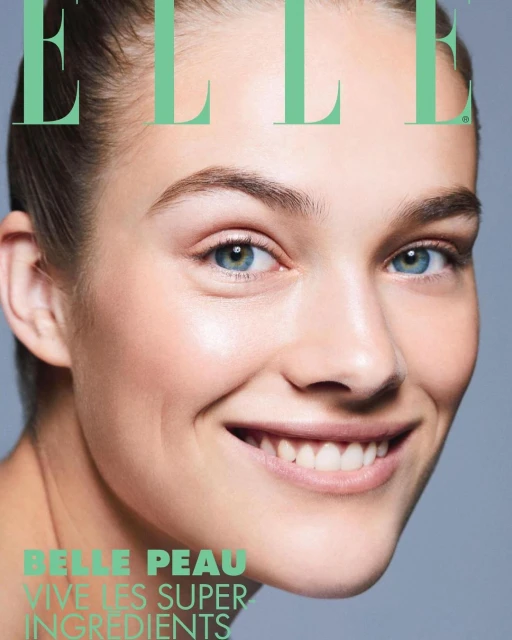 Close-up magazine cover featuring a smiling young woman with clear skin, blue eyes, and natural makeup, against a soft grey background.