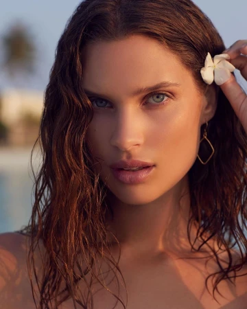 Close-up portrait of a woman with wet brown hair, blue eyes, and a white flower tucked behind her ear, photographed by Chris & Cory.