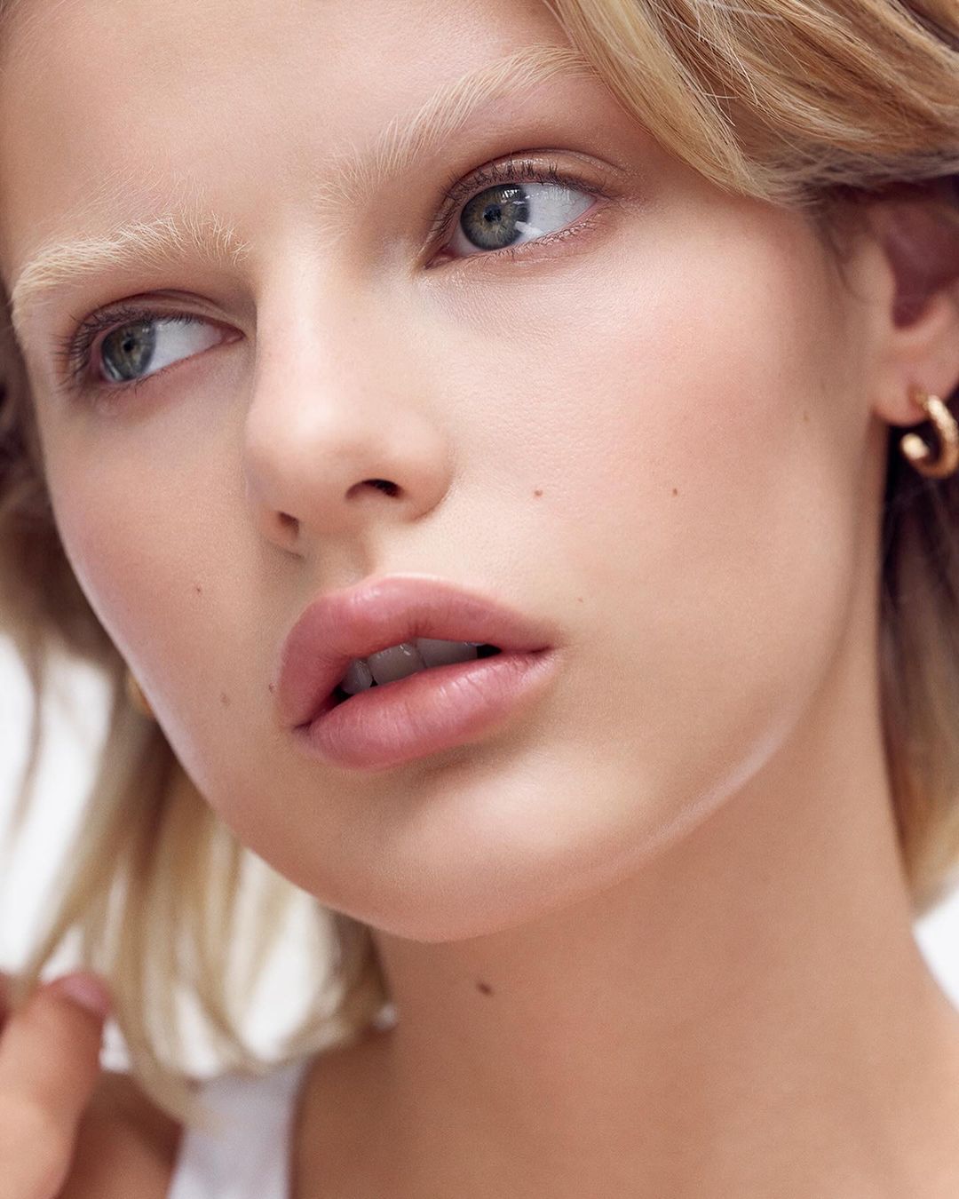 Close-up portrait of a blonde adult woman with light skin, wearing small gold hoop earrings. Beauty and fashion photography.