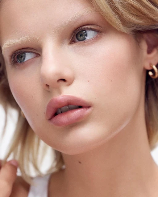 Close-up portrait of a blonde adult woman with light skin, wearing small gold hoop earrings. Beauty and fashion photography.