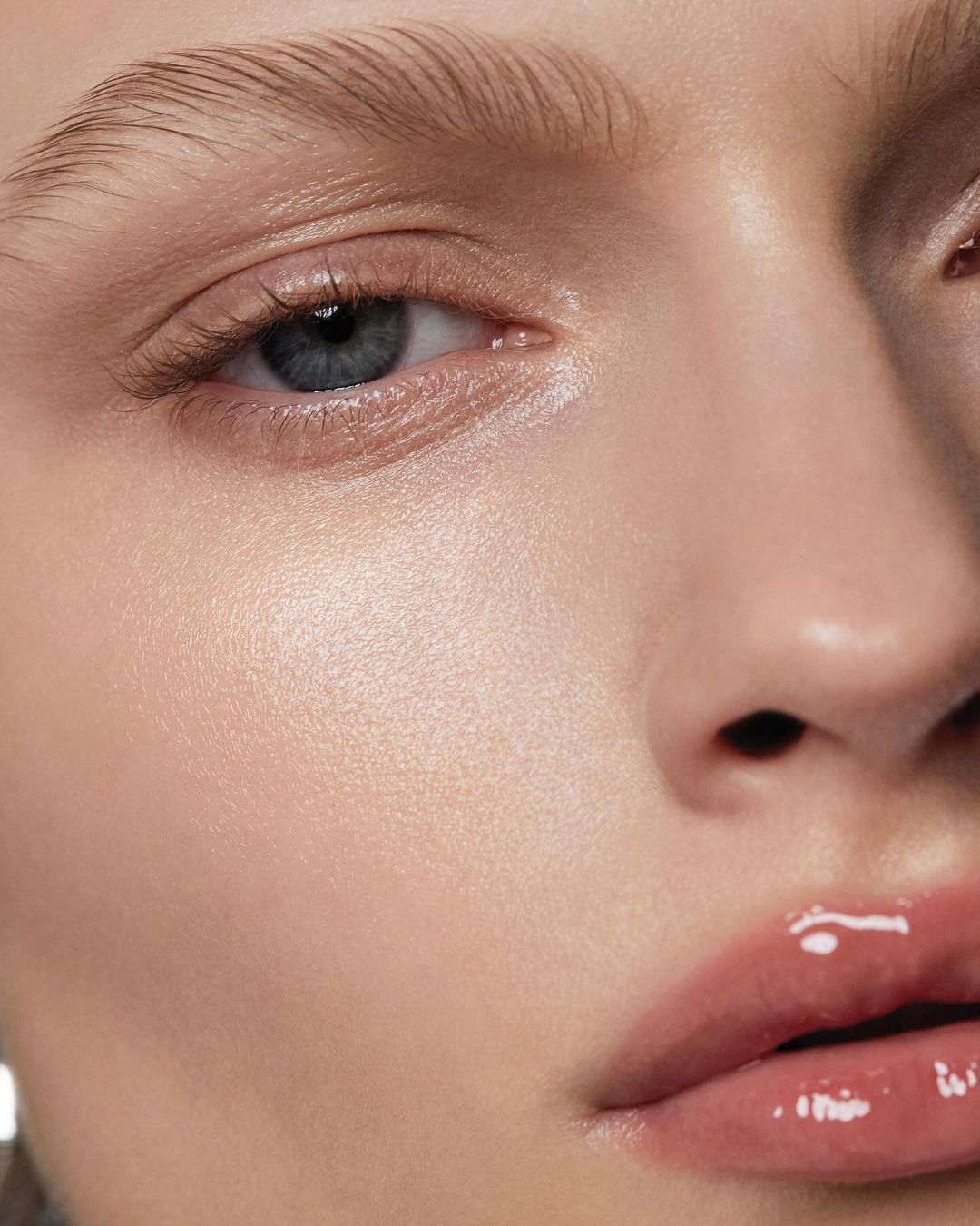 Close-up portrait of a woman's face featuring shiny lip gloss, prominent cheekbones, flawless skin, and a light complexion. Soft focus.