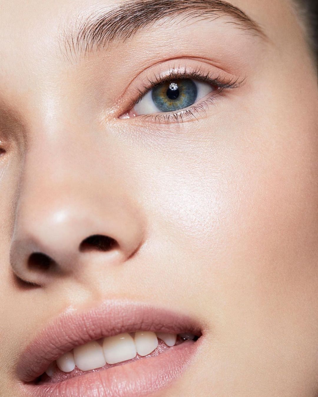 Close-up portrait of a young adult woman with blue eyes and fair skin, wearing light pink lipstick, with a neutral facial expression.