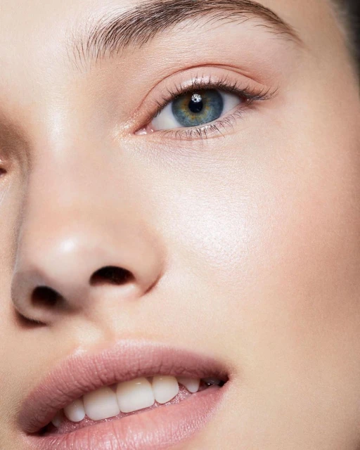 Close-up portrait of a young adult woman with blue eyes and fair skin, wearing light pink lipstick, with a neutral facial expression.