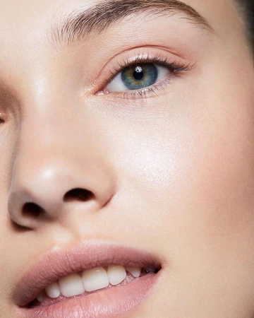 Close-up portrait of a young adult woman with blue eyes and fair skin, wearing light pink lipstick, with a neutral facial expression.