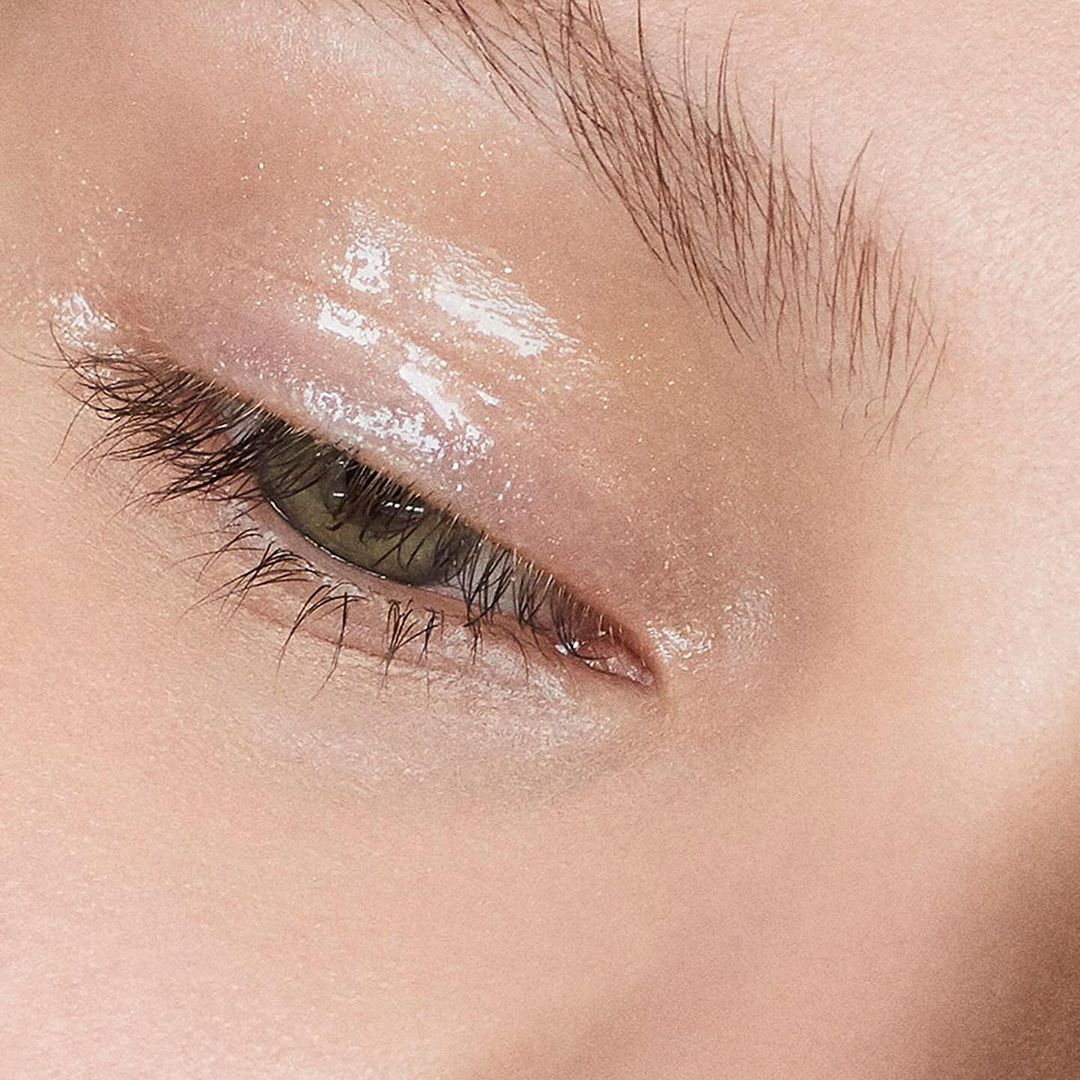 Close-up of a woman's face featuring a green eye with eyebrow, eyelashes, and reflective eye makeup. Perfect for beauty product advertising.