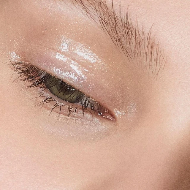 Close-up of a woman's face featuring a green eye with eyebrow, eyelashes, and reflective eye makeup. Perfect for beauty product advertising.