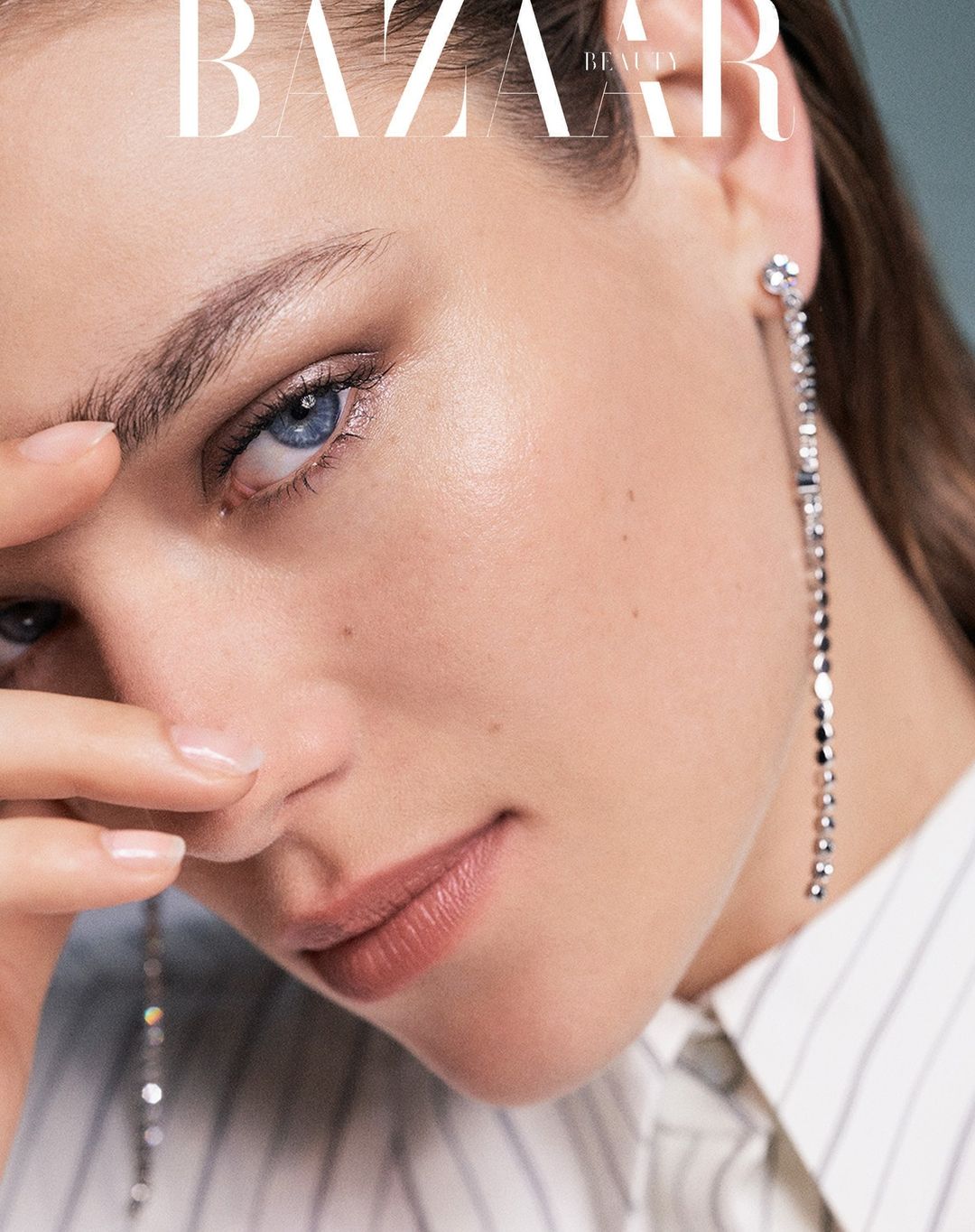 Close-up of a fair-skinned woman with blue eyes, wearing a white button-down shirt and long crystal earrings, and Bazaar Beauty text.