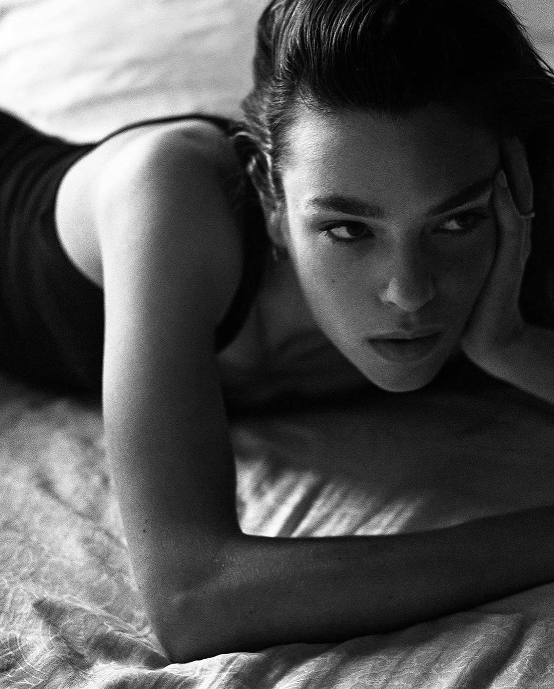 Monochrome portrait of a woman lying on a textured surface, resting her head on her hand, captured with a shallow depth of field.