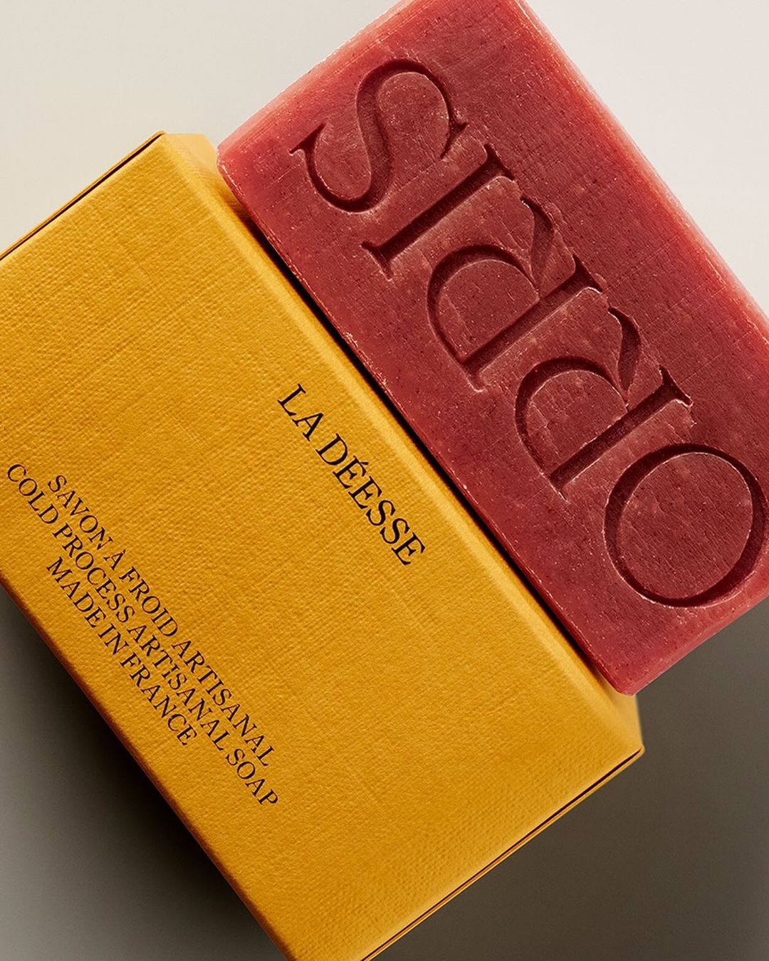 Artisanal soap bar with 'ORRIS' embossed in pink, resting on a yellow box labeled 'LA DÉESSE' with cold process details.