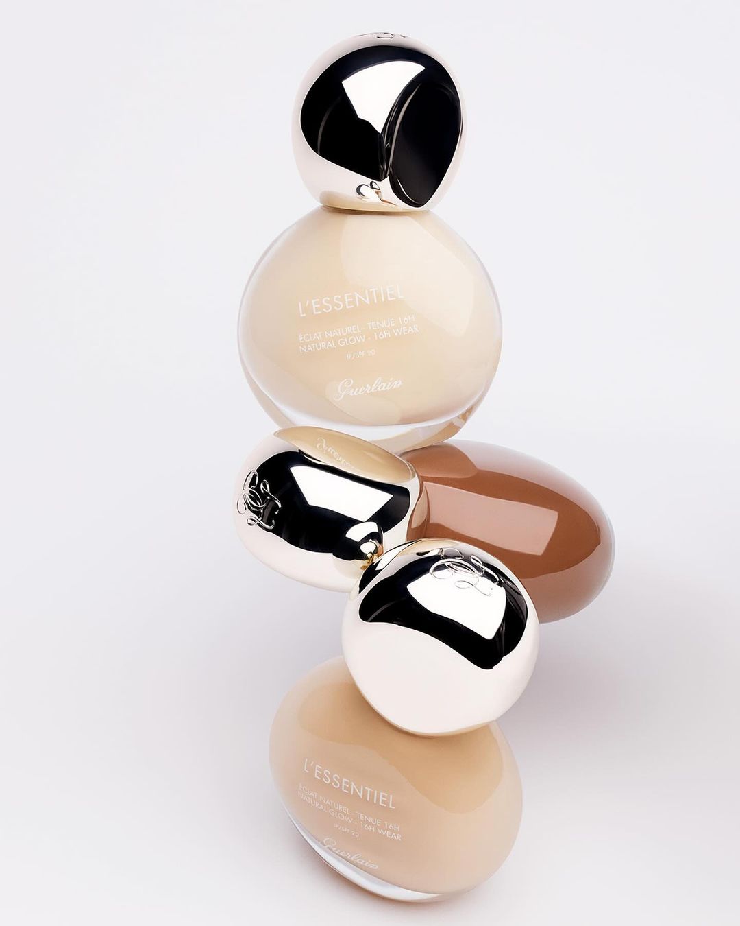 Close-up of beauty product bottles stacked vertically against a plain white background, featuring neutral and brown tones, and silver accents.
