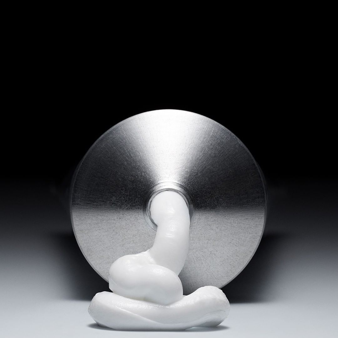 Close-up of a squeezed metal tube of white cream on a white surface against a dark backdrop in a studio setting. Product shot.