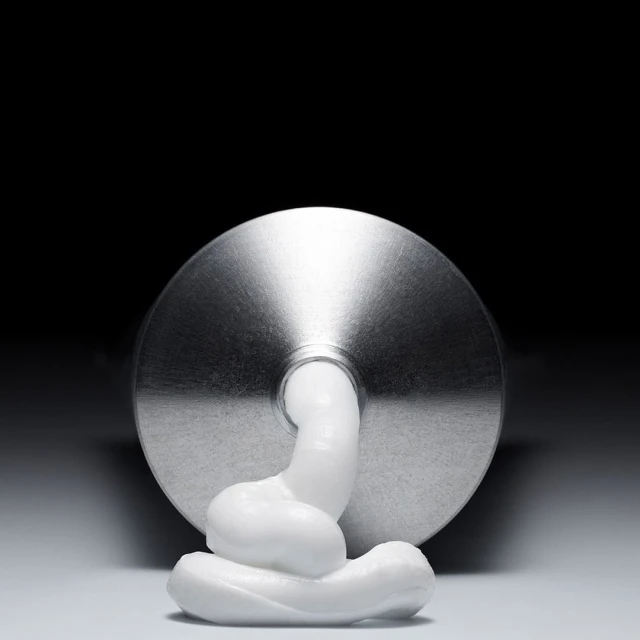 Close-up of a squeezed metal tube of white cream on a white surface against a dark backdrop in a studio setting. Product shot.