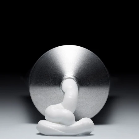 Close-up of a squeezed metal tube of white cream on a white surface against a dark backdrop in a studio setting. Product shot.