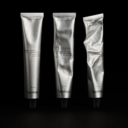 Three silver tubes of Typology hand cream are lined up against a dark background in a product shot showcasing minimalist beauty.