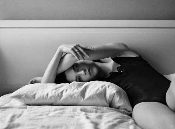 Monochrome portrait of a woman lying on a bed with her arms crossed above her head, captured in Dusseldorf by Chris & Cory.