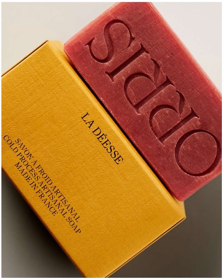 Artisanal soap bar with embossed 'ORRIS' text and its box labeled 'LA DEESSE'. The soap and box create a textured and contrasted image.