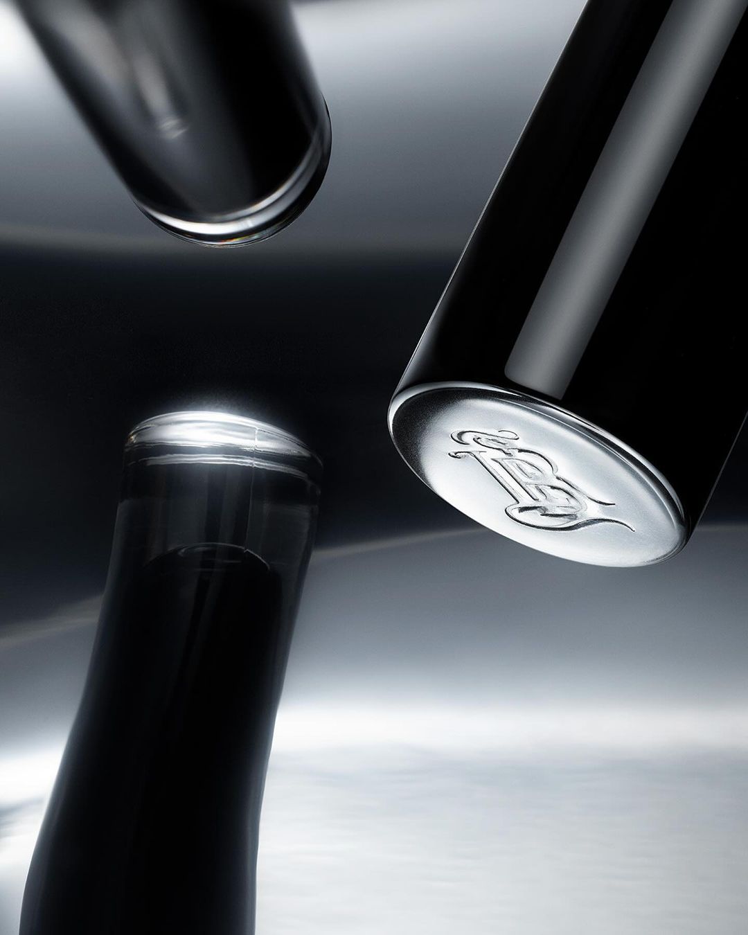 Three sleek, dark perfume bottles arranged on a reflective surface, creating a minimalist and elegant composition.