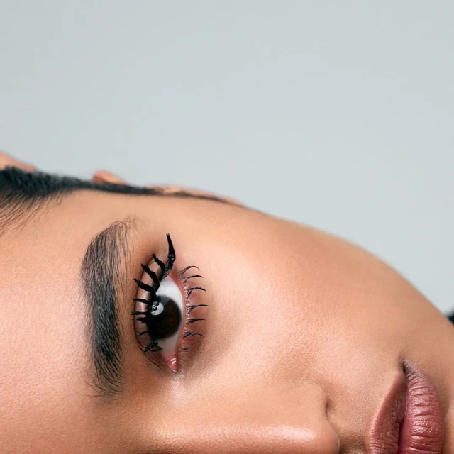 Close-up of a woman's eye with exaggerated black eyelashes on a grey background. Beauty shot for makeup, fashion, and design.