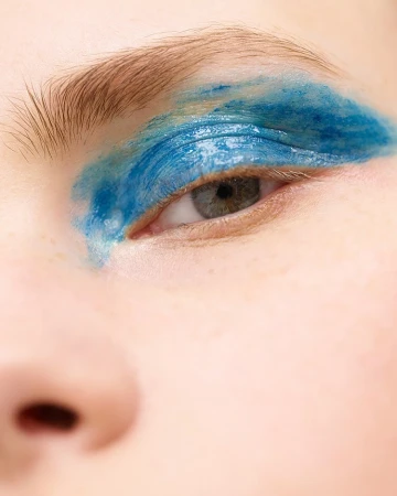 Close-up portrait of a person with expressive blue makeup smeared across their eyelid and eyebrow by photographers Chris and Cory.