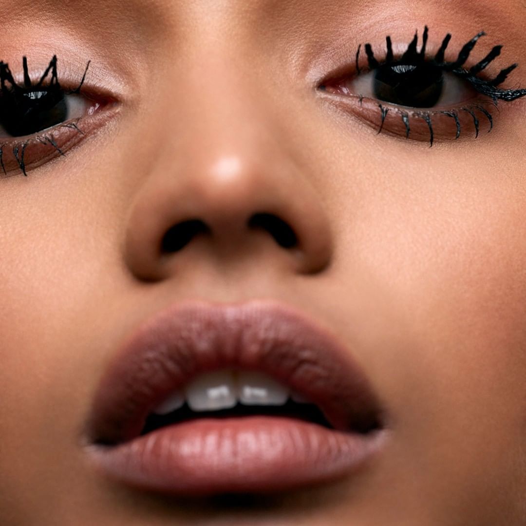 Extreme close-up of a woman's face: eyes with thick mascara, nose, and full lips, creating an intimate and detailed beauty shot.