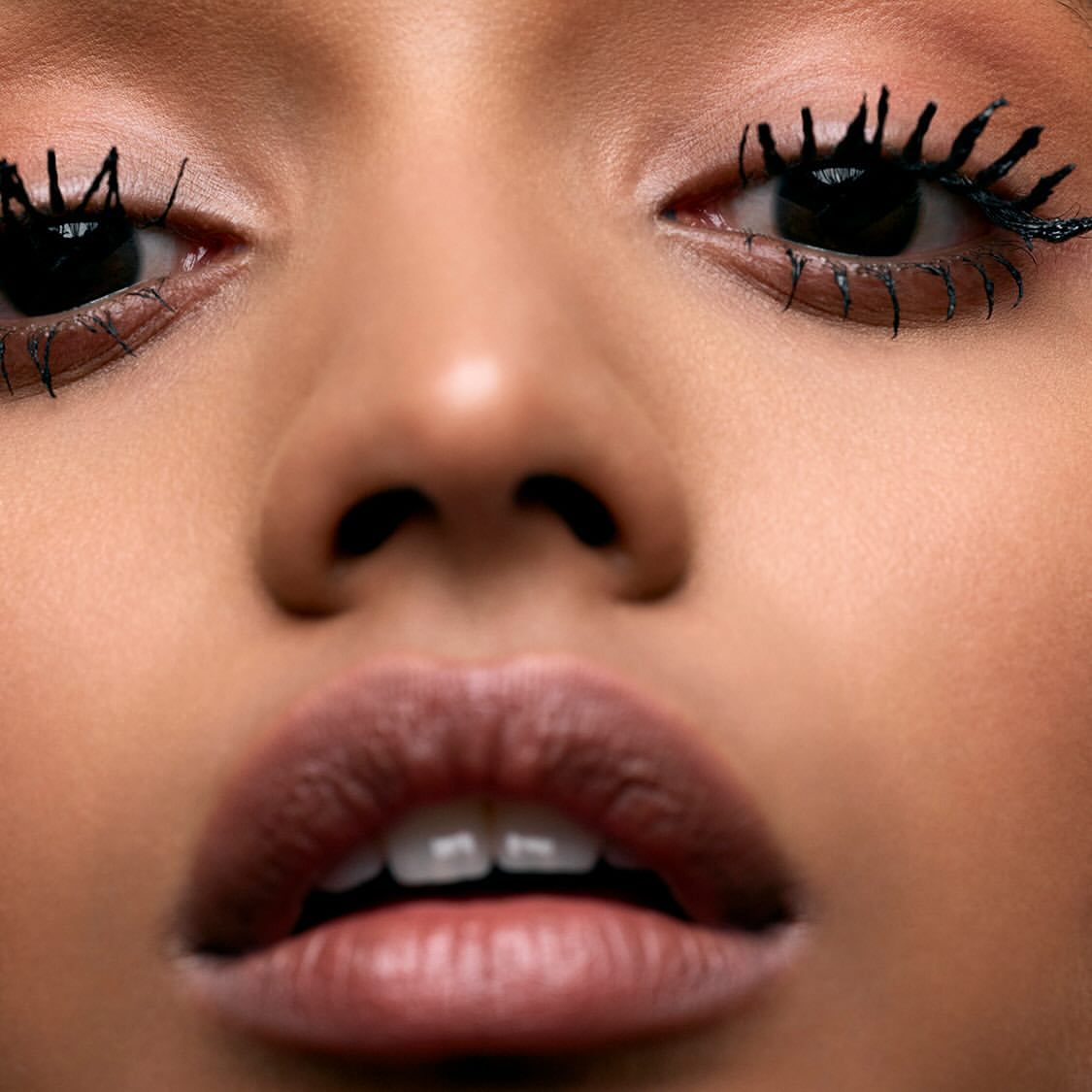 Extreme close-up of an adult woman's face, featuring dramatic eyelashes with thick mascara, glossy lips, and fair skin tone.