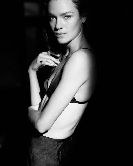 Striking black and white portrait of a woman in lingerie with dramatic lighting emphasizing her face and figure in a dark setting.