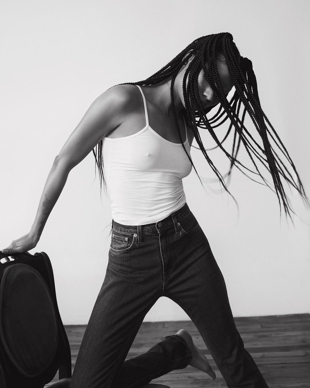 Black and white portrait of a woman with long braided hair whipping through the air while wearing a tank top and jeans.