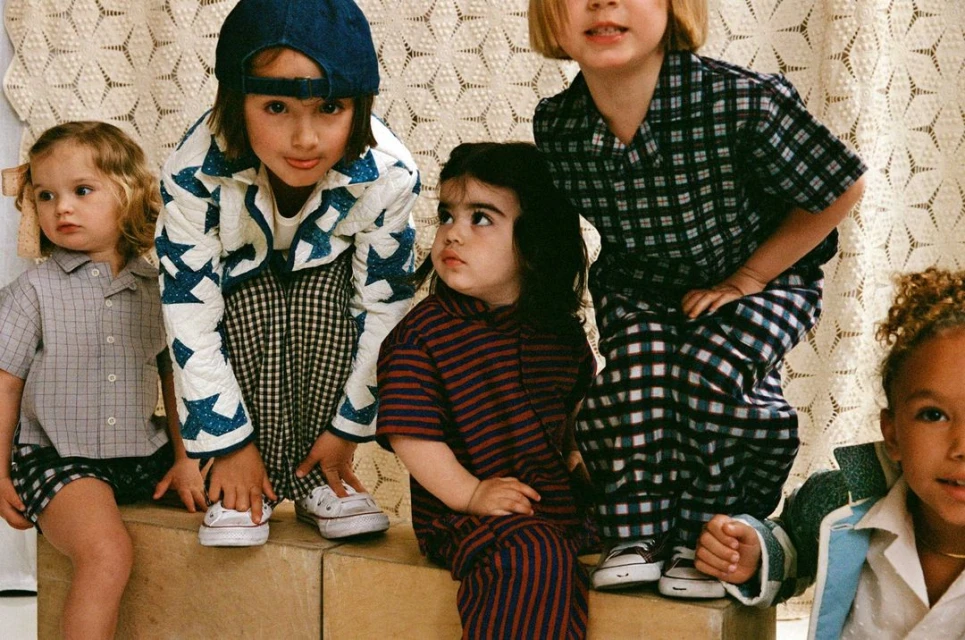Group of five young children in patterned clothing sit on blocks indoors, posing for a portrait in a casual, indoor setting.