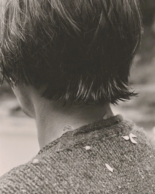 Close up shot of an adult with dark hair wearing a knit sweater with petals scattered across it, against a neutral backdrop.