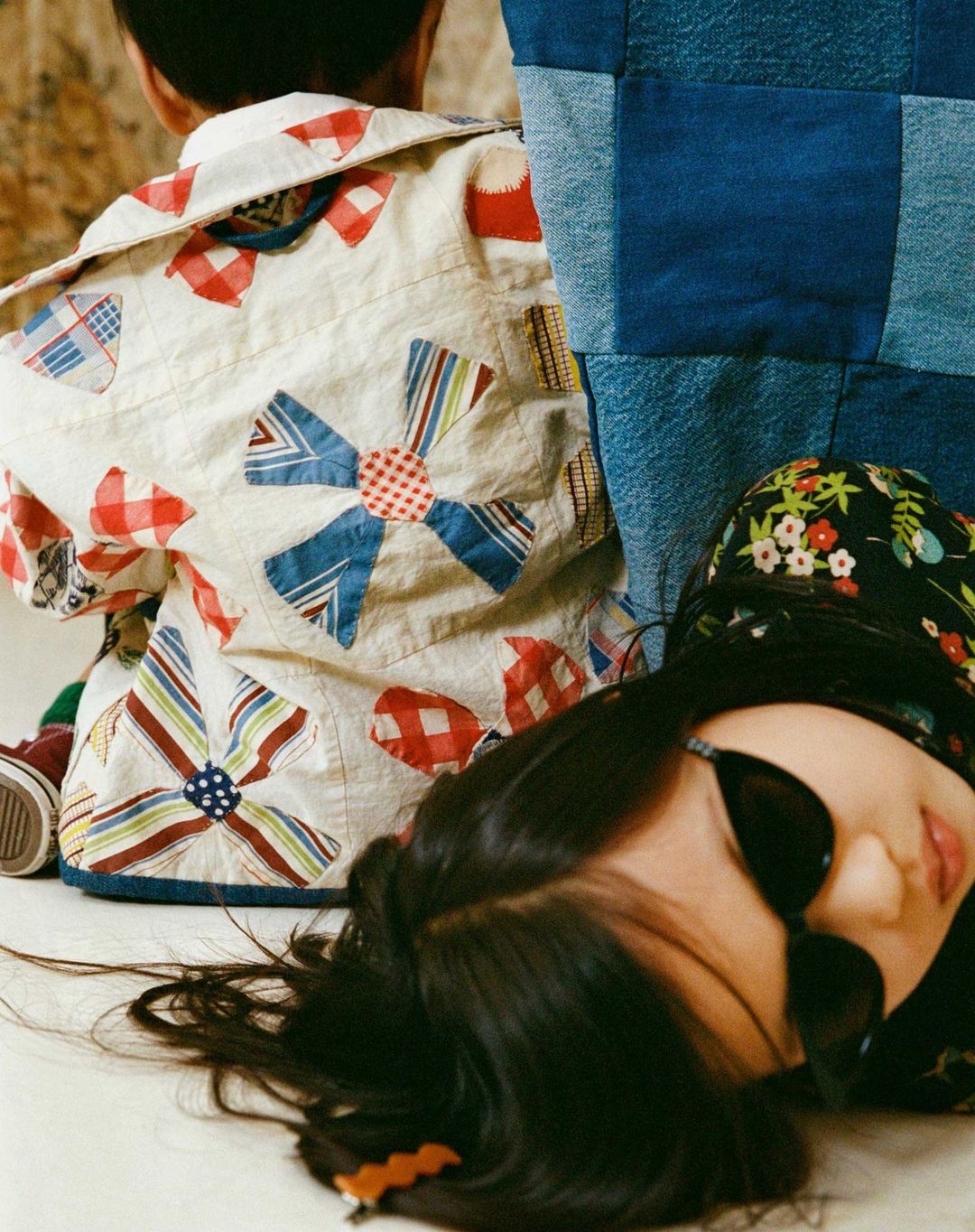 Two children are featured in a studio setting, one lying down and the other sitting, both dressed in colorful, patterned tops.