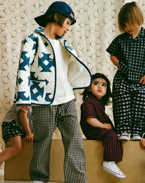 Four children model a quilted jacket, checked pants, and matching checked pajamas in a playful and stylish indoor fashion shoot.