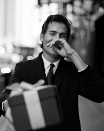 Black and white portrait of a smiling man holding out a wrapped gift box toward the camera in New York.