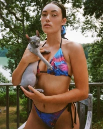 Woman wearing a blue and pink bikini holding a hairless Sphynx cat on a balcony by Chris Bernabeo