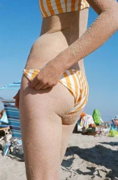 Close-up of a woman wearing a yellow and white striped bikini dusted with sand on a sunny beach