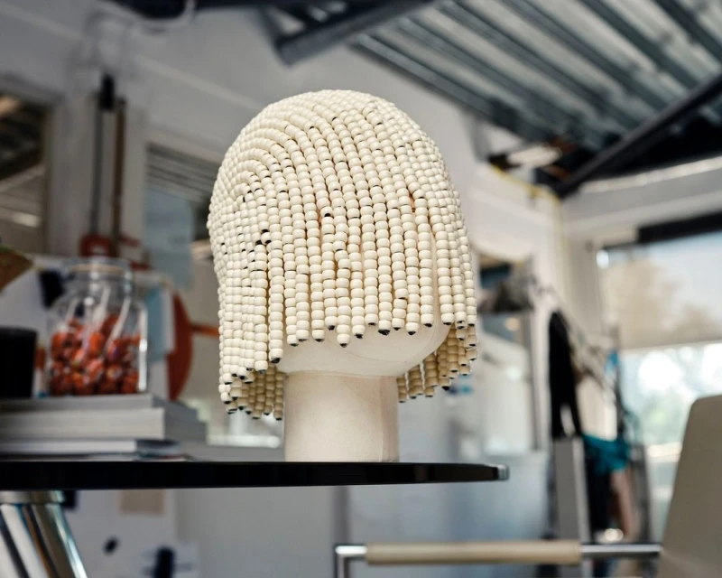 Unique beaded wig on display. Beadwork fashion hairpiece on a black shelf, set against an interior backdrop.