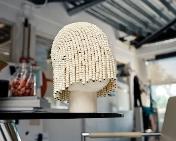 Unique beaded wig on display. Beadwork fashion hairpiece on a black shelf, set against an interior backdrop.