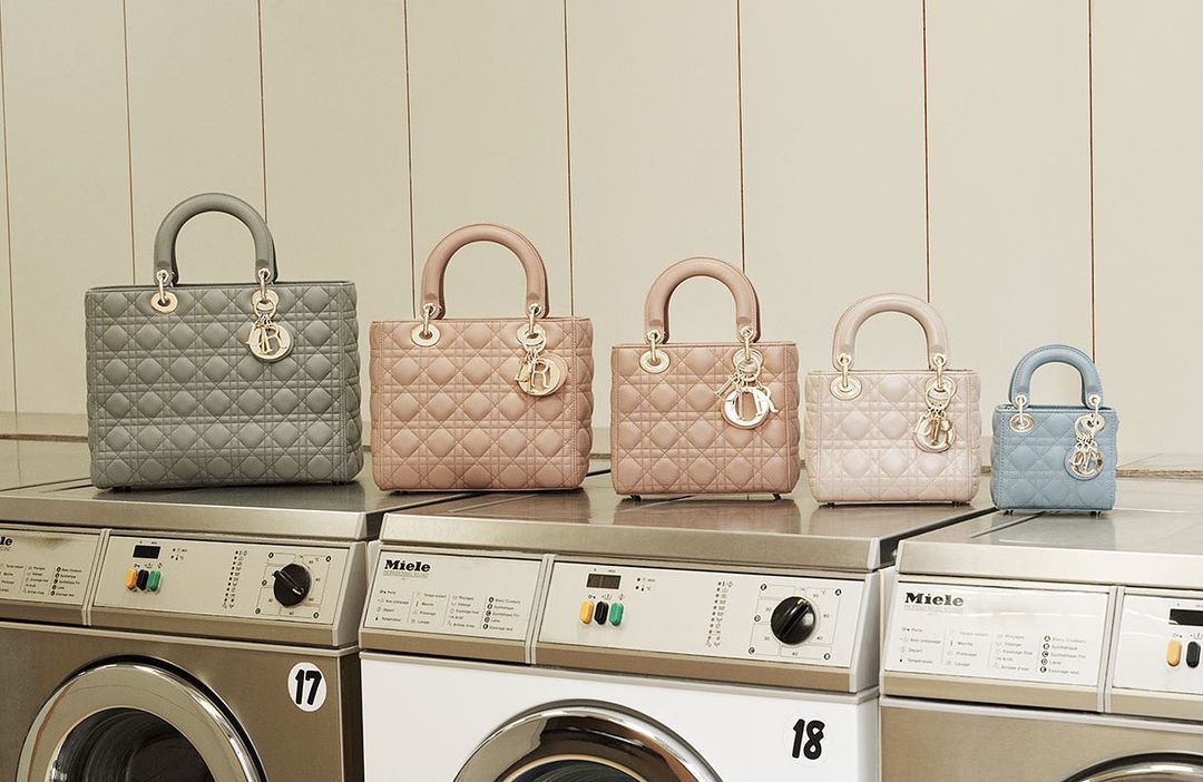 Five luxury quilted leather handbags with top handles arranged on top of stainless steel Miele washing machines in a laundry room setting.